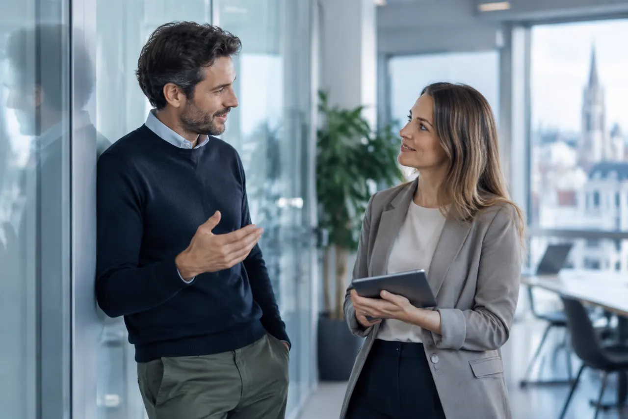 Two professionals talking beside a glass wall in a modern workspace, illustrating partnership